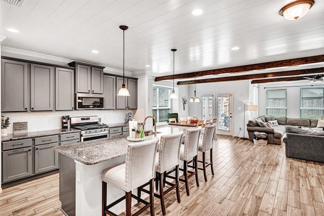 kitchen with open floor plan, gray cabinets, stainless steel appliances, a kitchen bar, and backsplash