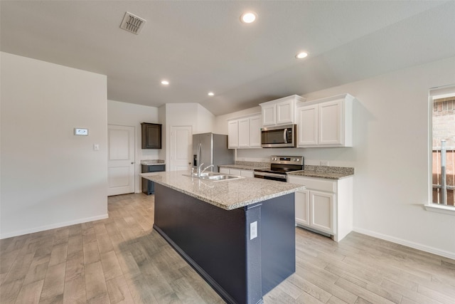 kitchen with an island with sink, light wood finished floors, stainless steel appliances, and a sink