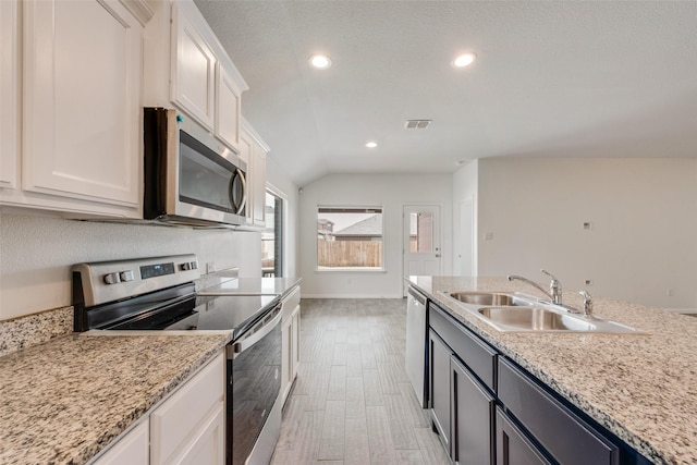 kitchen with stainless steel appliances, a sink, visible vents, white cabinetry, and vaulted ceiling