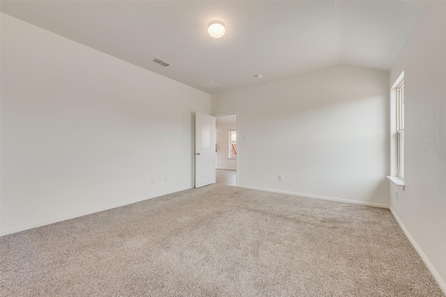 carpeted empty room featuring visible vents, vaulted ceiling, and baseboards