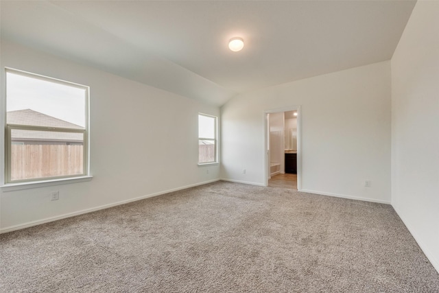 carpeted spare room featuring vaulted ceiling and baseboards