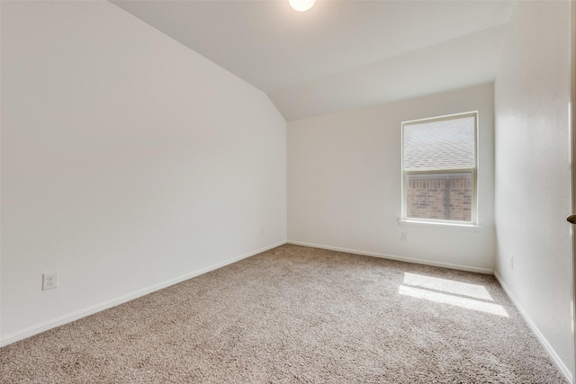 carpeted empty room featuring lofted ceiling and baseboards