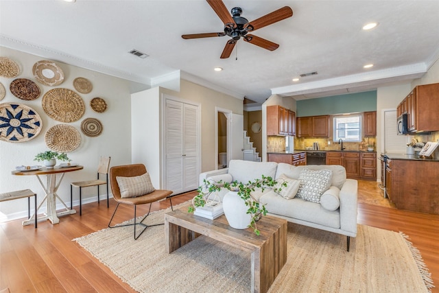 living area featuring baseboards, visible vents, a ceiling fan, ornamental molding, and light wood-type flooring