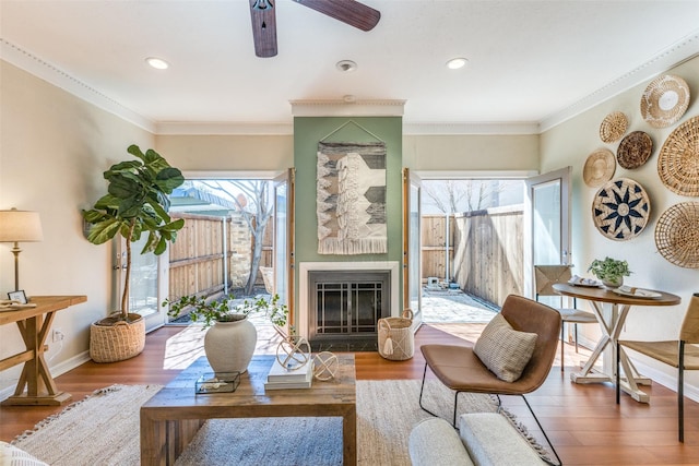 living room with crown molding, baseboards, wood finished floors, and a glass covered fireplace