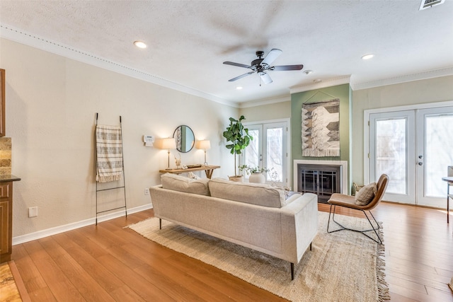 living room featuring french doors, light wood finished floors, ornamental molding, a glass covered fireplace, and baseboards