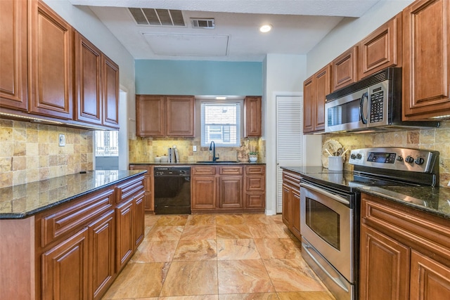 kitchen featuring stainless steel appliances, visible vents, a sink, and dark stone countertops