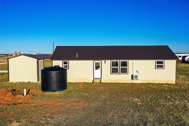 back of house featuring an outbuilding, entry steps, ac unit, a lawn, and metal roof