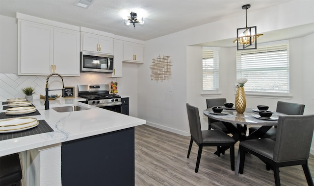kitchen with a sink, light wood-type flooring, appliances with stainless steel finishes, a notable chandelier, and visible vents