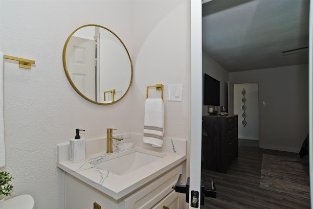 half bathroom with toilet, a textured wall, vanity, and wood finished floors