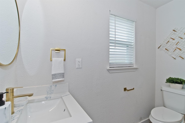 half bathroom featuring a textured wall, vanity, and toilet