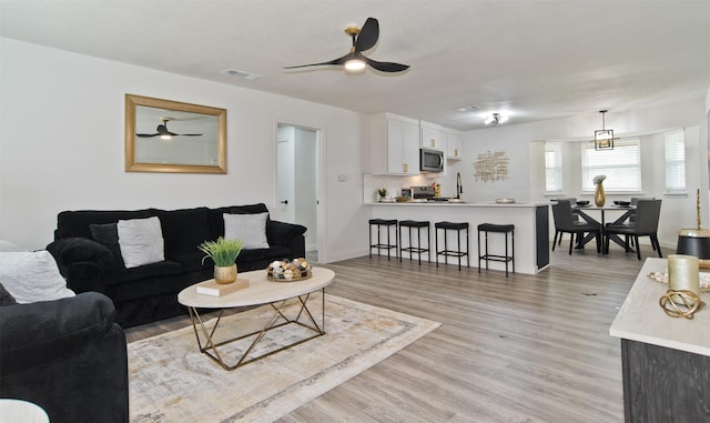 living area featuring light wood-style flooring, visible vents, baseboards, and ceiling fan