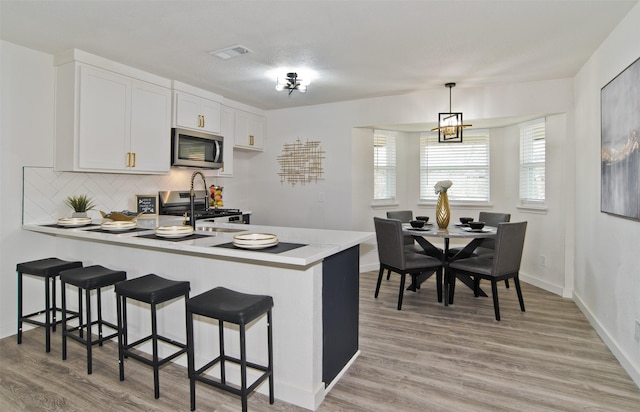 kitchen with a kitchen breakfast bar, tasteful backsplash, a peninsula, appliances with stainless steel finishes, and visible vents