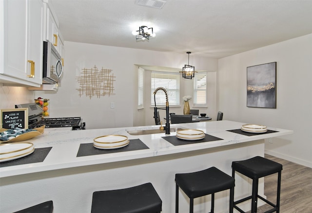 kitchen featuring wood finished floors, a sink, a kitchen bar, white cabinets, and appliances with stainless steel finishes