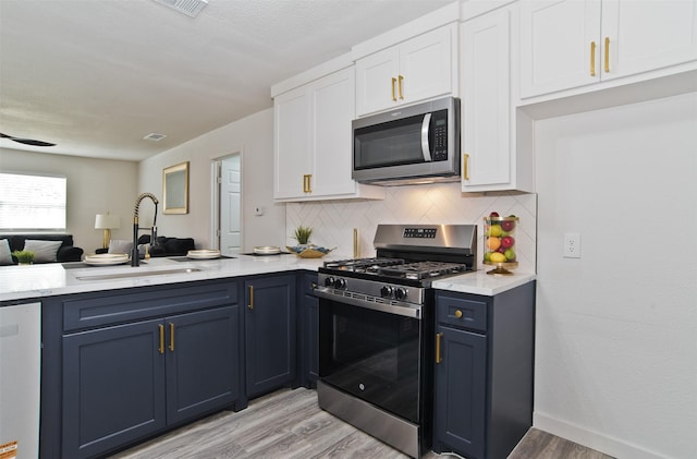 kitchen featuring a sink, stainless steel appliances, light wood finished floors, light countertops, and white cabinets