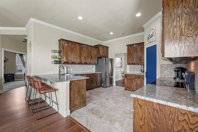 kitchen with light stone counters, a breakfast bar area, visible vents, freestanding refrigerator, and a peninsula