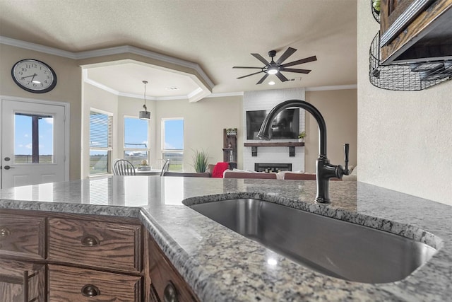 kitchen featuring a healthy amount of sunlight, a large fireplace, ornamental molding, and a sink