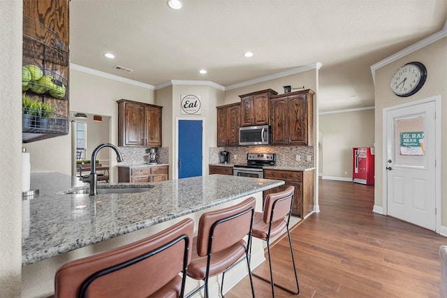 kitchen featuring light stone counters, wood finished floors, a sink, visible vents, and appliances with stainless steel finishes