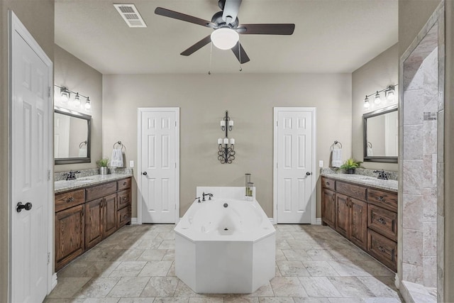 full bathroom featuring two vanities, a garden tub, visible vents, and stone tile floors