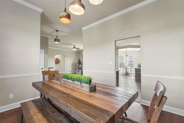 dining room with ornamental molding, arched walkways, baseboards, and wood finished floors