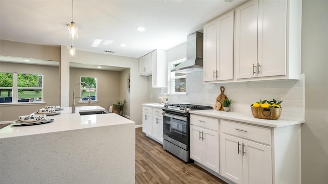 kitchen with decorative backsplash, a sink, wall chimney range hood, wood finished floors, and stainless steel gas range oven