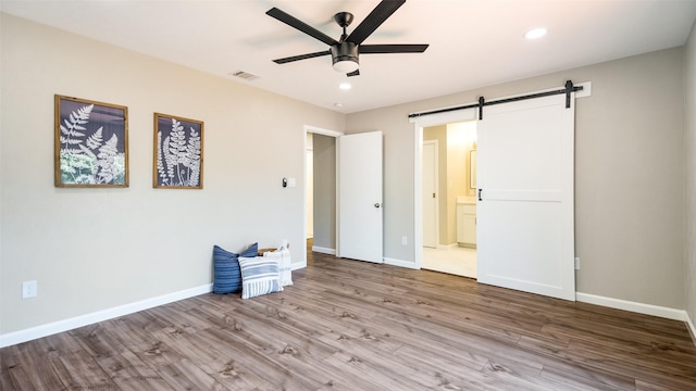 unfurnished bedroom with baseboards, a barn door, visible vents, and wood finished floors