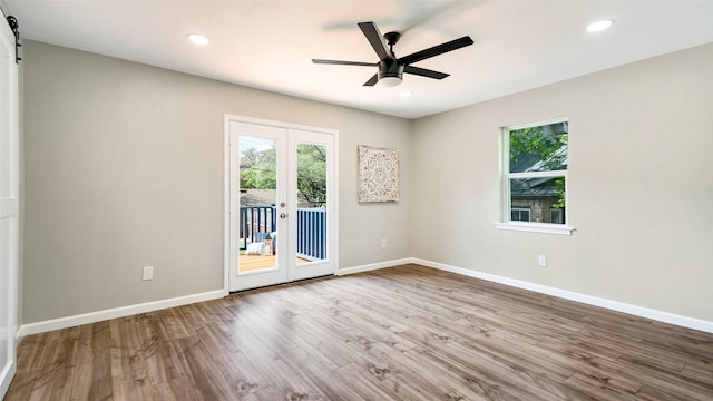 empty room with ceiling fan, a barn door, wood finished floors, baseboards, and french doors