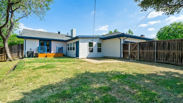 rear view of property featuring a lawn, a fenced backyard, a chimney, a deck, and brick siding