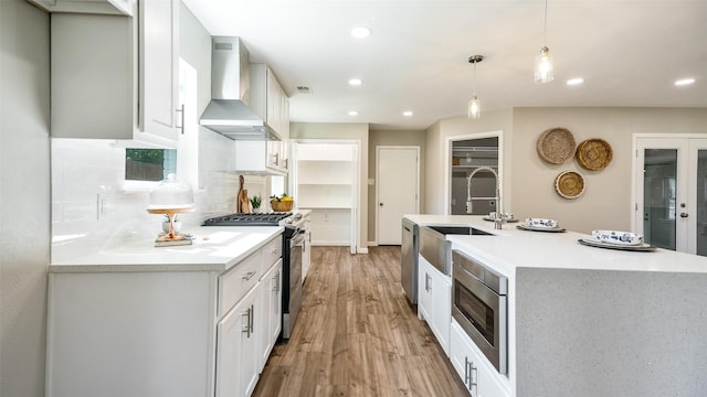 kitchen featuring stainless steel appliances, a sink, light wood-type flooring, backsplash, and wall chimney exhaust hood