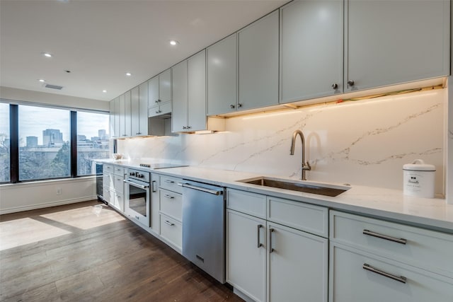 kitchen with light stone counters, dark wood-style floors, a sink, decorative backsplash, and stainless steel appliances