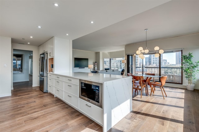 kitchen featuring white cabinetry, freestanding refrigerator, an inviting chandelier, light wood finished floors, and built in microwave