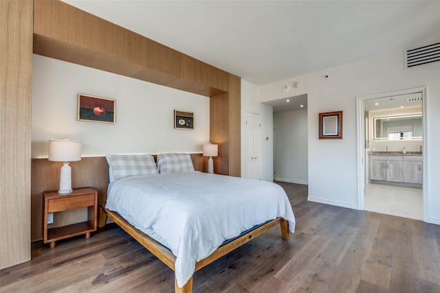 bedroom with ensuite bath, wood finished floors, visible vents, and baseboards