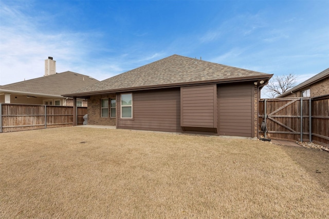 back of house with brick siding, a shingled roof, fence, a yard, and a gate