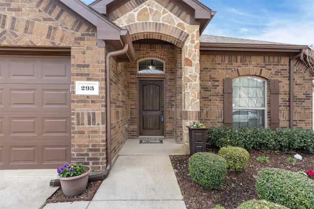 entrance to property featuring an attached garage, stone siding, a shingled roof, and brick siding