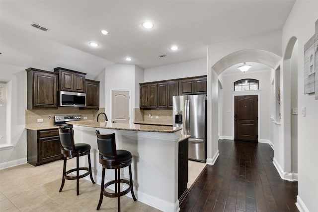 kitchen featuring arched walkways, appliances with stainless steel finishes, visible vents, and dark brown cabinetry