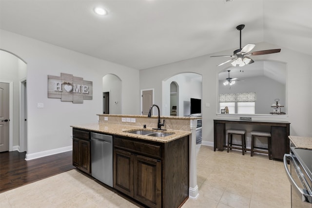 kitchen with arched walkways, appliances with stainless steel finishes, vaulted ceiling, a sink, and dark brown cabinets