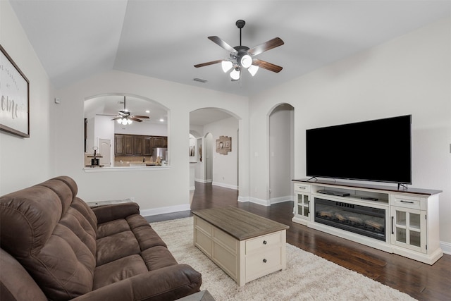 living area with ceiling fan, arched walkways, wood finished floors, visible vents, and vaulted ceiling