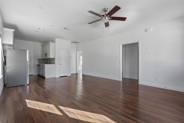 unfurnished living room with dark wood-style floors, visible vents, baseboards, and a ceiling fan