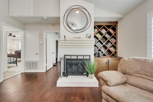 sitting room with visible vents, dark wood-type flooring, vaulted ceiling, a textured ceiling, and a brick fireplace