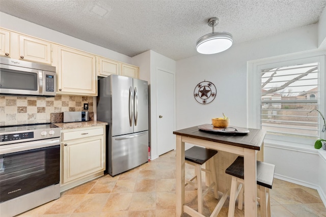 kitchen featuring decorative light fixtures, stainless steel appliances, backsplash, cream cabinets, and a textured ceiling