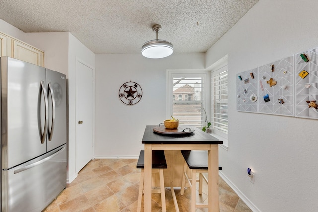 kitchen featuring a textured ceiling, freestanding refrigerator, and baseboards