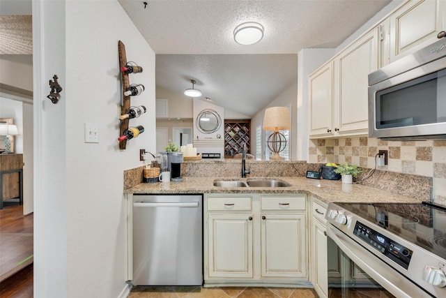 kitchen with lofted ceiling, a sink, stainless steel appliances, cream cabinetry, and backsplash