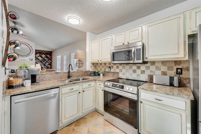 kitchen featuring tasteful backsplash, lofted ceiling, appliances with stainless steel finishes, cream cabinetry, and a sink