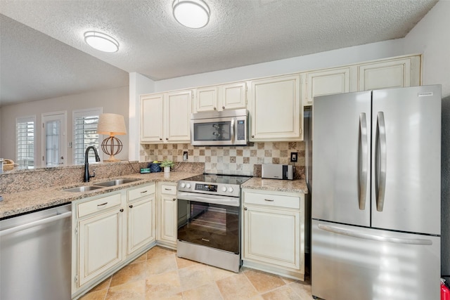 kitchen with stainless steel appliances, cream cabinets, a sink, and decorative backsplash