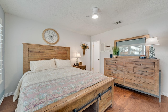 bedroom with a textured ceiling, dark wood-type flooring, visible vents, and baseboards