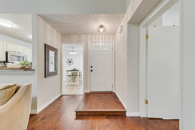 entryway with wood-type flooring, a textured ceiling, and baseboards