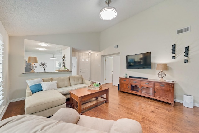 living area featuring light wood-style flooring, a textured ceiling, visible vents, and baseboards