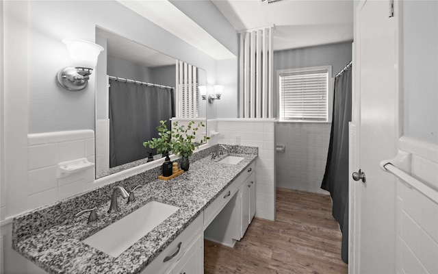 full bath featuring a wainscoted wall, wood finished floors, a sink, and tile walls