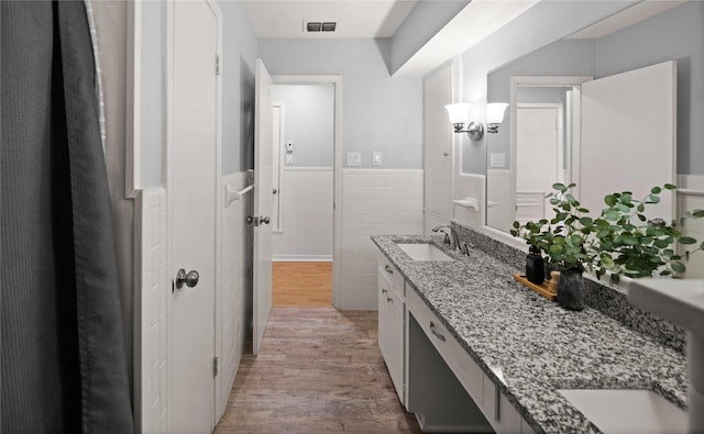 bathroom with a wainscoted wall, tile walls, visible vents, a sink, and wood finished floors