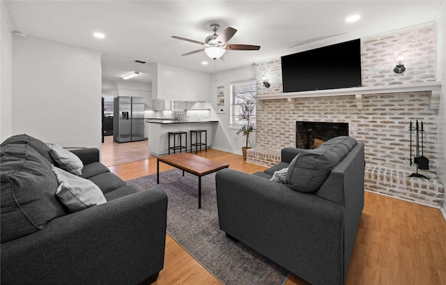 living area featuring a ceiling fan, recessed lighting, a brick fireplace, and light wood finished floors