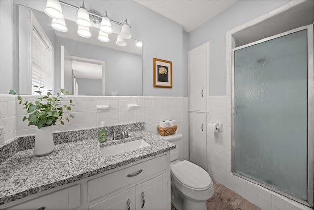 full bath featuring tile walls, toilet, a stall shower, wainscoting, and vanity